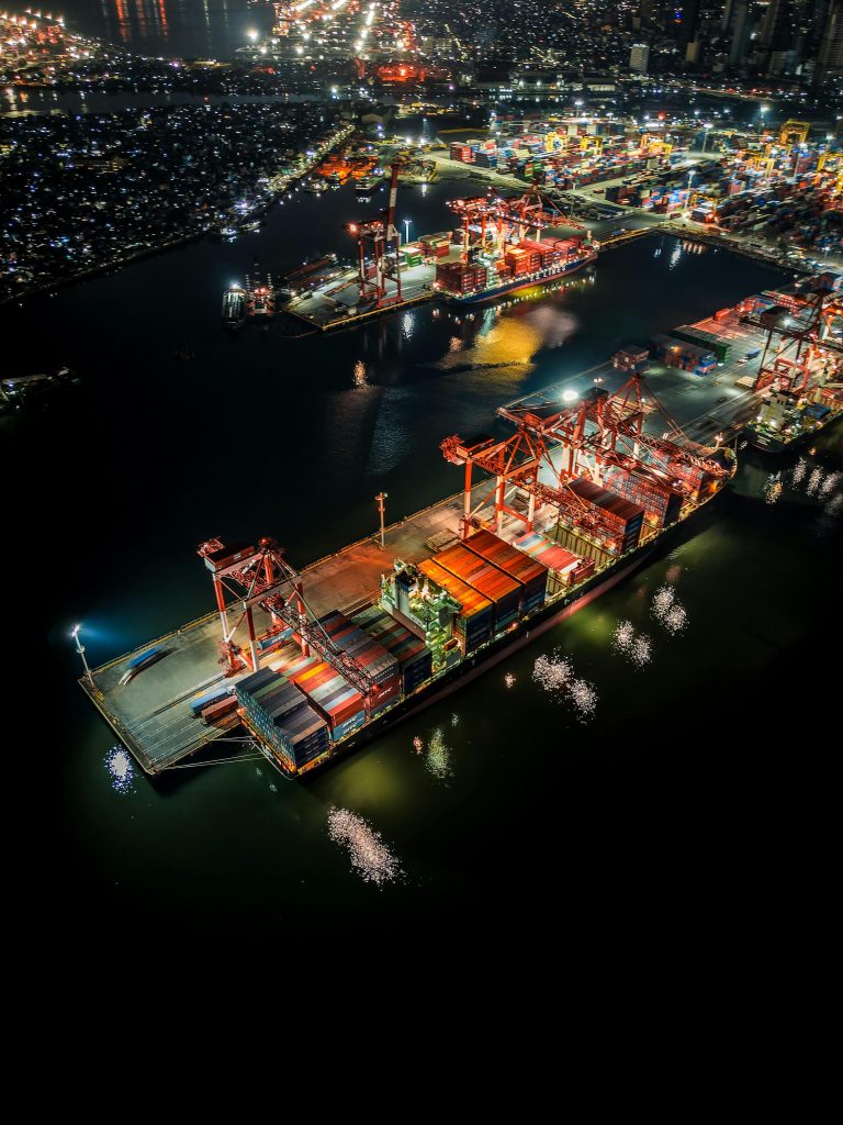 Aerial night view of an illuminated container port showcasing bustling activity and vibrant city lights.